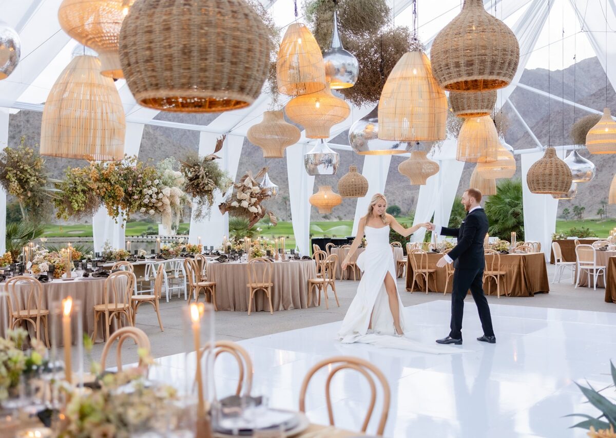 Bride and groom share a dance on a white floor under wicker lanterns at an elegant outdoor wedding reception.