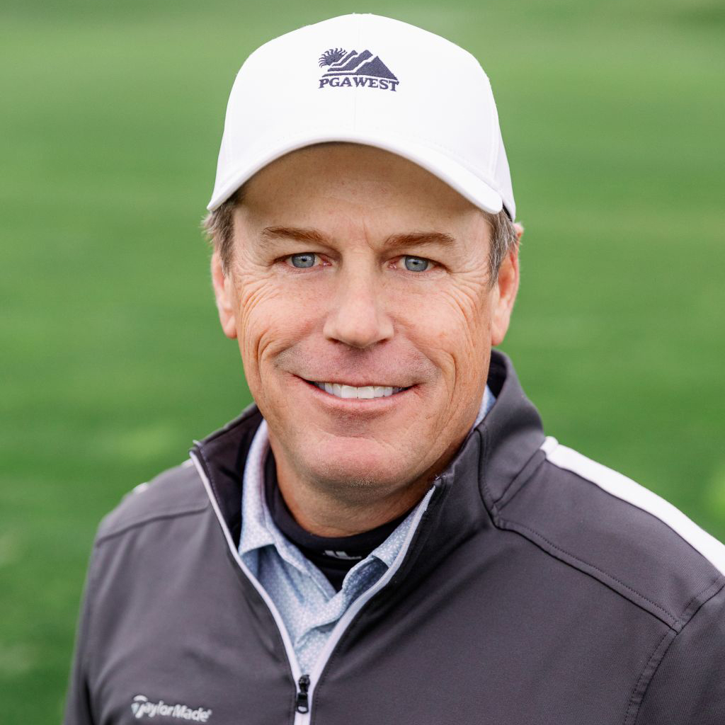 Man in a PGA West hat and jacket smiling on a golf course.